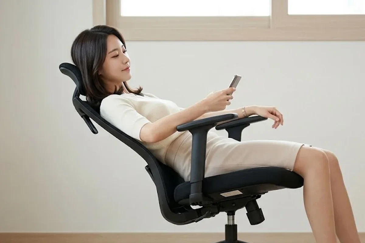등받이를 젖힌 사무용 의자에 등 전체를 붙이고 팔걸이에 팔을 얹은 채 휴대폰을 보며 쉬는 옆모습